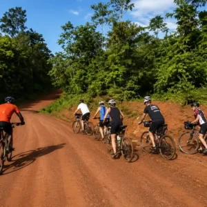 Een groep mountainbikers fietst over een brede, onverharde rode zandweg omringd door dicht tropisch bos.