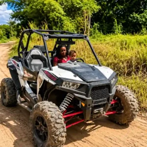 Een vrouw en een jong kind rijden in een stoere, wit-zwarte UTV buggy over een onverharde zandweg in Suriname.